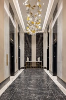 Un vestíbulo moderno con pisos de mármol, una mesa central y un elemento decorativo colgante.