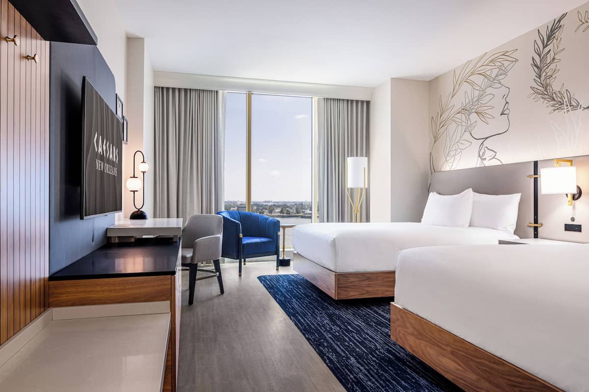 A hotel room with a large bed, a desk with a chair, a TV, and a view of the city.