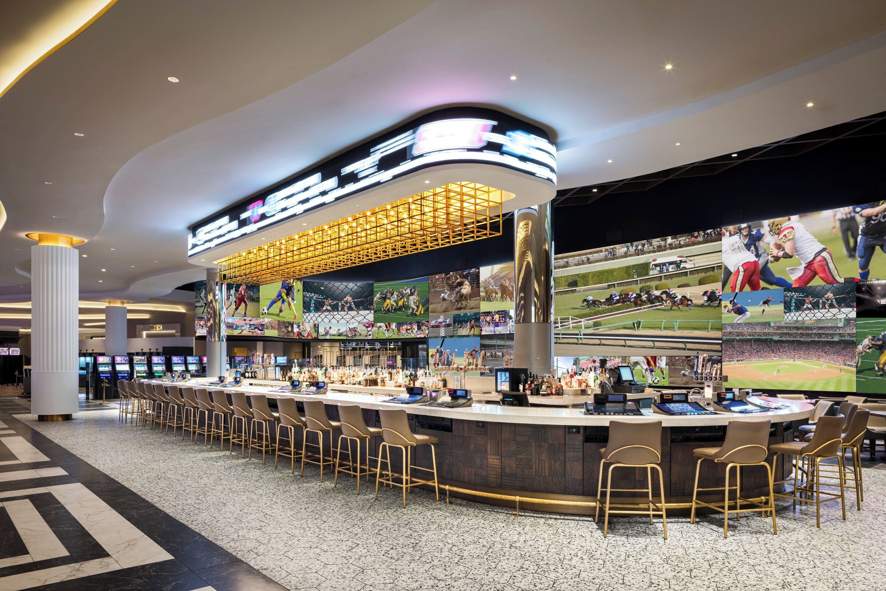 A bar area with multiple screens displaying sports events, bar stools, and a counter with a digital display.