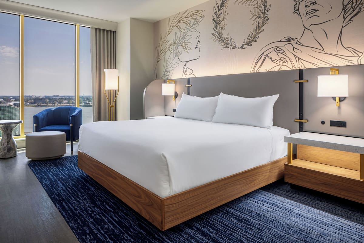 A hotel room with a large bed, bedside lamps, a chair, and a view of the city.