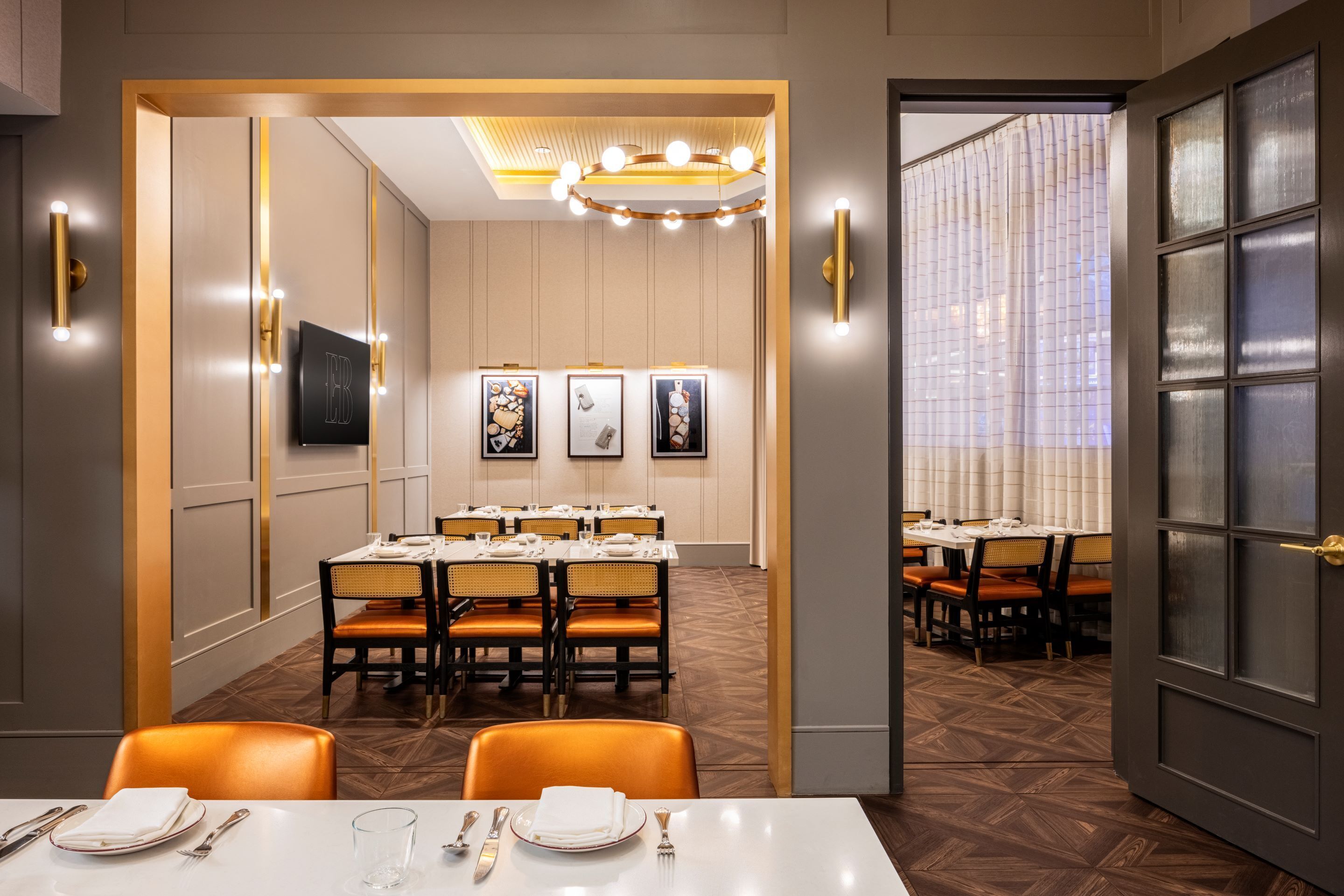 A hotel dining area with tables set for service, a chandelier, framed artwork on the walls, and a patterned floor.