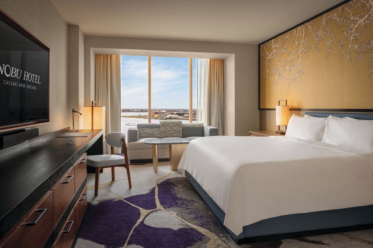 A hotel room with a bed, a desk, a chair, a TV, a window with curtains, and a view of the city.