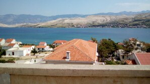 Un pueblo costero con casas de tejados terracota, un mar azul cristalino y montañas a lo lejos.