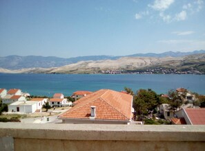 Eine Küstenstadt mit terrakottafarbenen Dächern, blauem Meer und Bergen im Hintergrund.