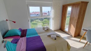 A bedroom with two beds, a wooden wardrobe, a desk, and a window with a view of buildings and greenery. - Villa Horizont - Four Bedroom Villa with Sea View (Fazana)