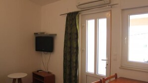 A room with a wooden dining table, a small white table, a television mounted on the wall, and a sliding glass door with a curtain.
