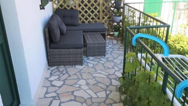 A stone-floored patio with a sofa and two side tables, a green metal railing, and potted plants. - Apartments Kao Nekad - Two bedrom apartment (Primosten)