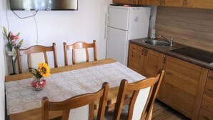 A compact kitchen with wooden cabinets, a white refrigerator, a built-in sink, and a flat-screen TV mounted on the wall. - Apartments Kao Nekad - Two bedrom apartment (Primosten)