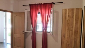 A room with a wooden door, a window with red curtains, and a wooden wardrobe.