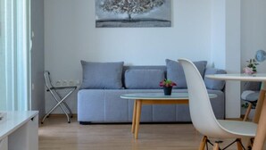Ein modernes Wohnzimmer mit einem grauen Sofa, einem Glastisch und einem weißen Sessel.