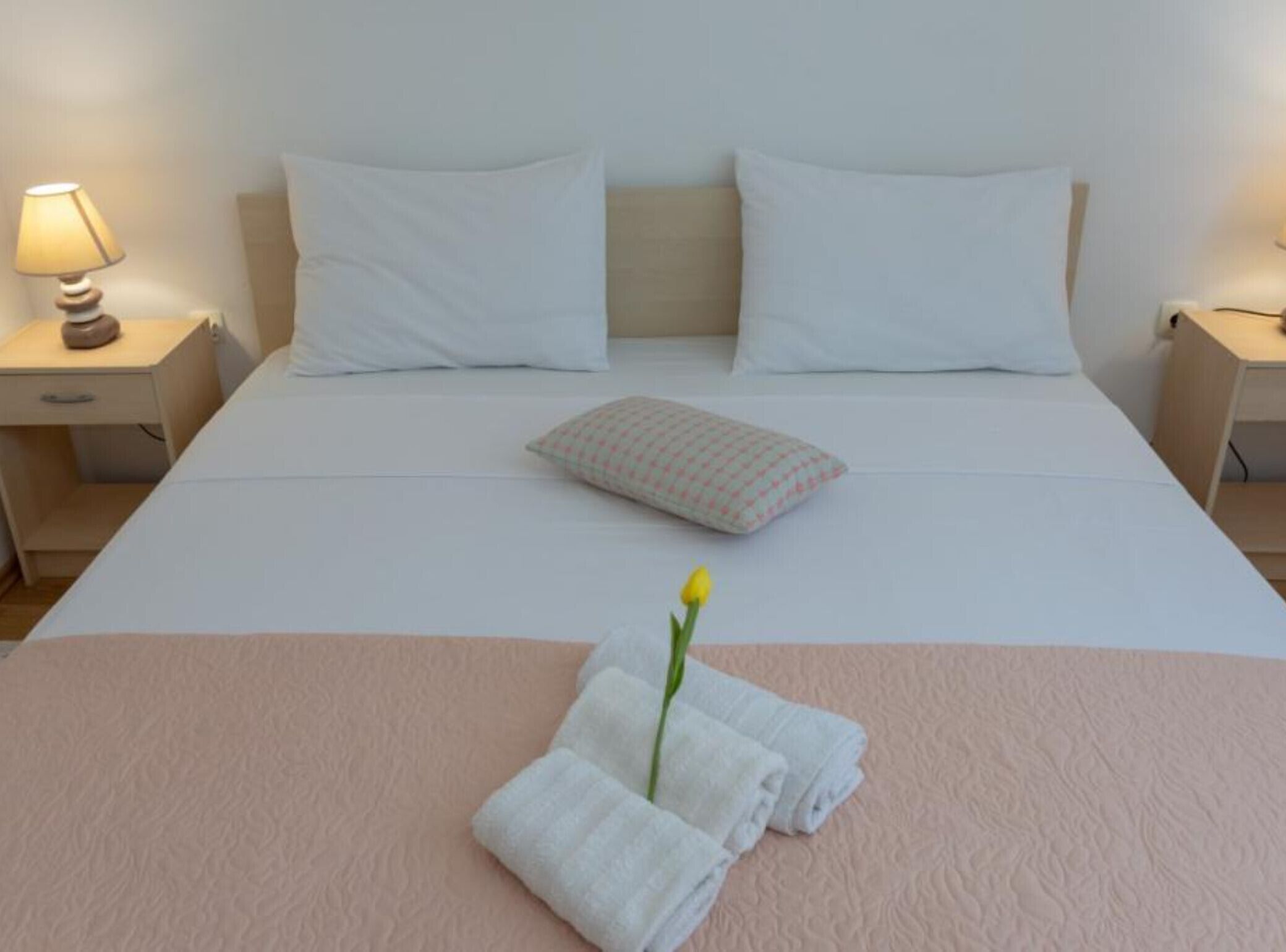 A neatly made bed with white linens, a single decorative pillow, and a small bouquet of flowers.