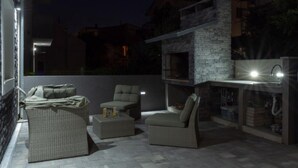 Ein Außenbereich mit Terrasse, Korbmöbeln, einer Steinwand und einer integrierten Küchenzeile mit Spüle und Beleuchtung.