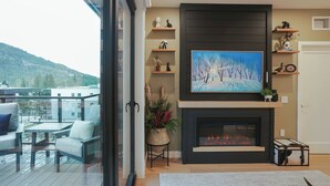 A modern living room with a fireplace, a large painting, and a balcony with outdoor furniture. - Big Hill Penthouse Chalet (Revelstoke)