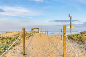 Ein sandiger Strandweg mit Holzbefestigungen und einem Seilzaun, der zum Meer führt.