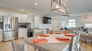 Una cocina moderna con armarios blancos, electrodomésticos de acero inoxidable y un comedor con mesa y sillas de madera.