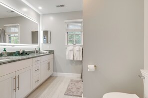 Une salle de bain moderne avec un grand miroir, des meubles blancs, un comptoir en marbre et des toilettes.