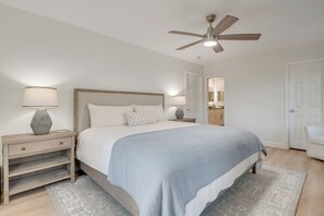 Une chambre à coucher comprenant un lit, des tables de chevet, un ventilateur de plafond et une porte donnant sur une autre pièce.
