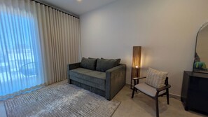 A living room with a sofa, a chair, a floor lamp, and a television. - Vista Cortes 2BR 2BA Condo - Walk to the Malecon! (La Paz)