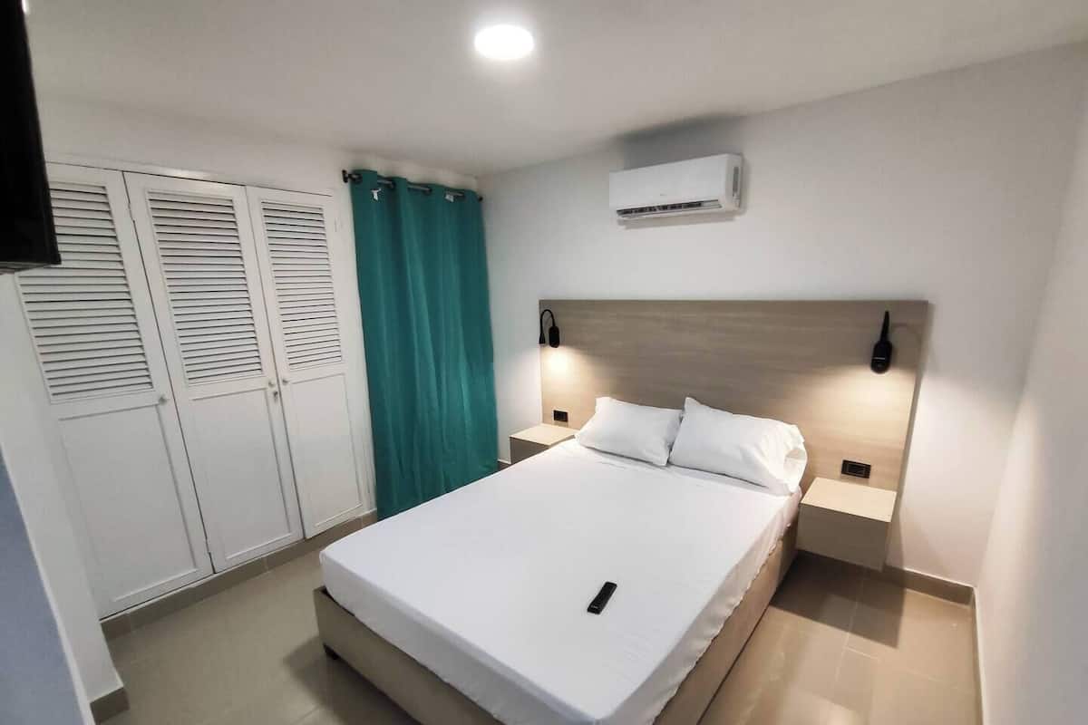 Un dormitorio ordenado con cama, armario, cortina, unidad de aire acondicionado y lámparas de noche.