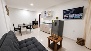 A modern living room with a sofa, a wooden coffee table, a kitchen area with cabinets and a refrigerator, and a TV mounted on the wall. - Edificio Los Manglares  (Cartagena)