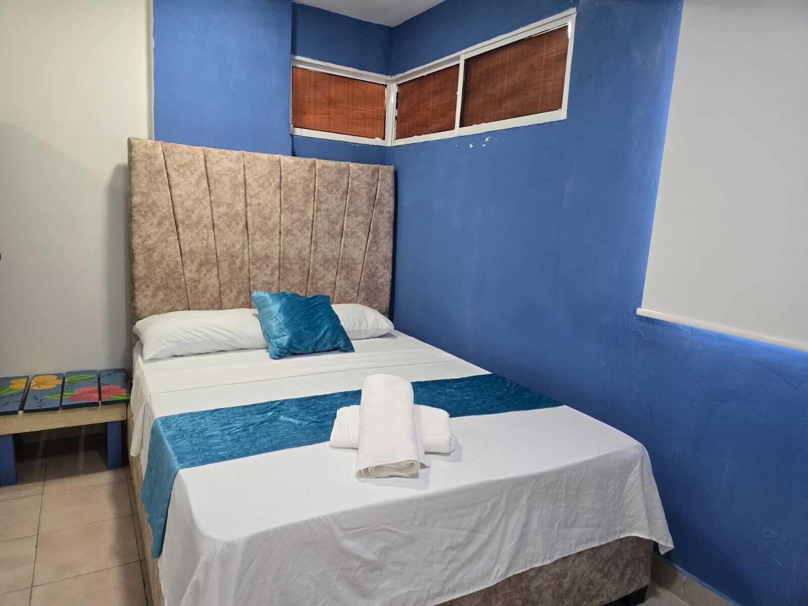 Ein Schlafzimmer mit einem Bett, einem Nachttisch, einem Fenster und einer blauen Wand.