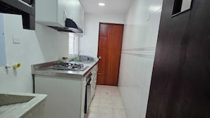 A narrow kitchen with a gas stove, a sink, and cabinets. - Edificio Los Manglares  (Cartagena)