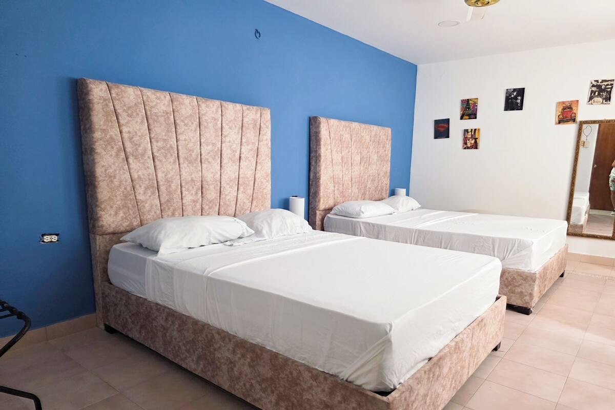 Habitación de hotel con dos camas, una pared azul y un espejo.