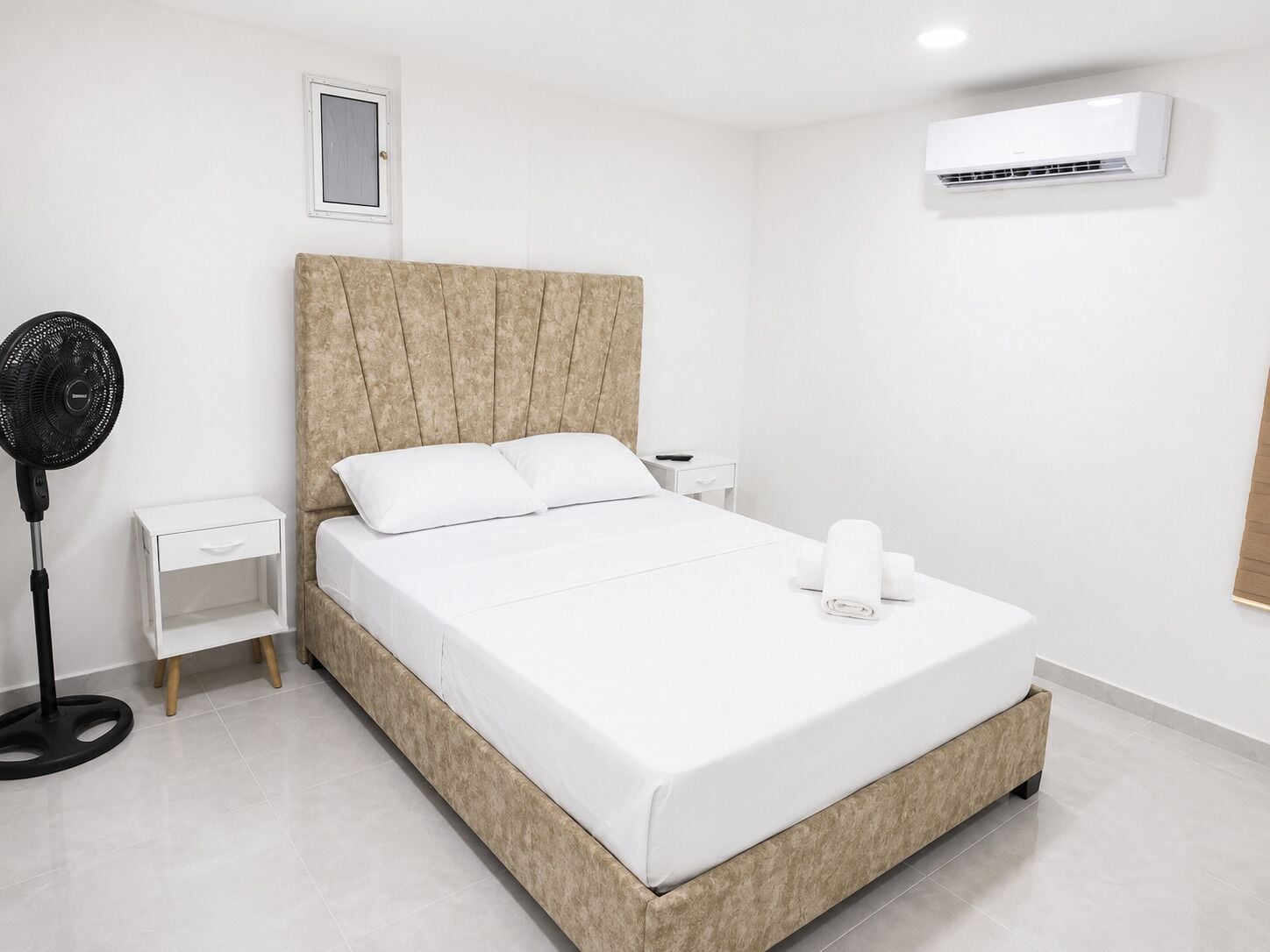 Ein modernes Schlafzimmer mit einem großen Bett, einem Nachttisch, einem Ventilator und einer Klimaanlage.
