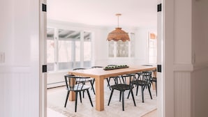 A dining area with a wooden table, black chairs, a woven pendant light, and a white rug. - Stay at Good Harbor Beach (Gloucester)