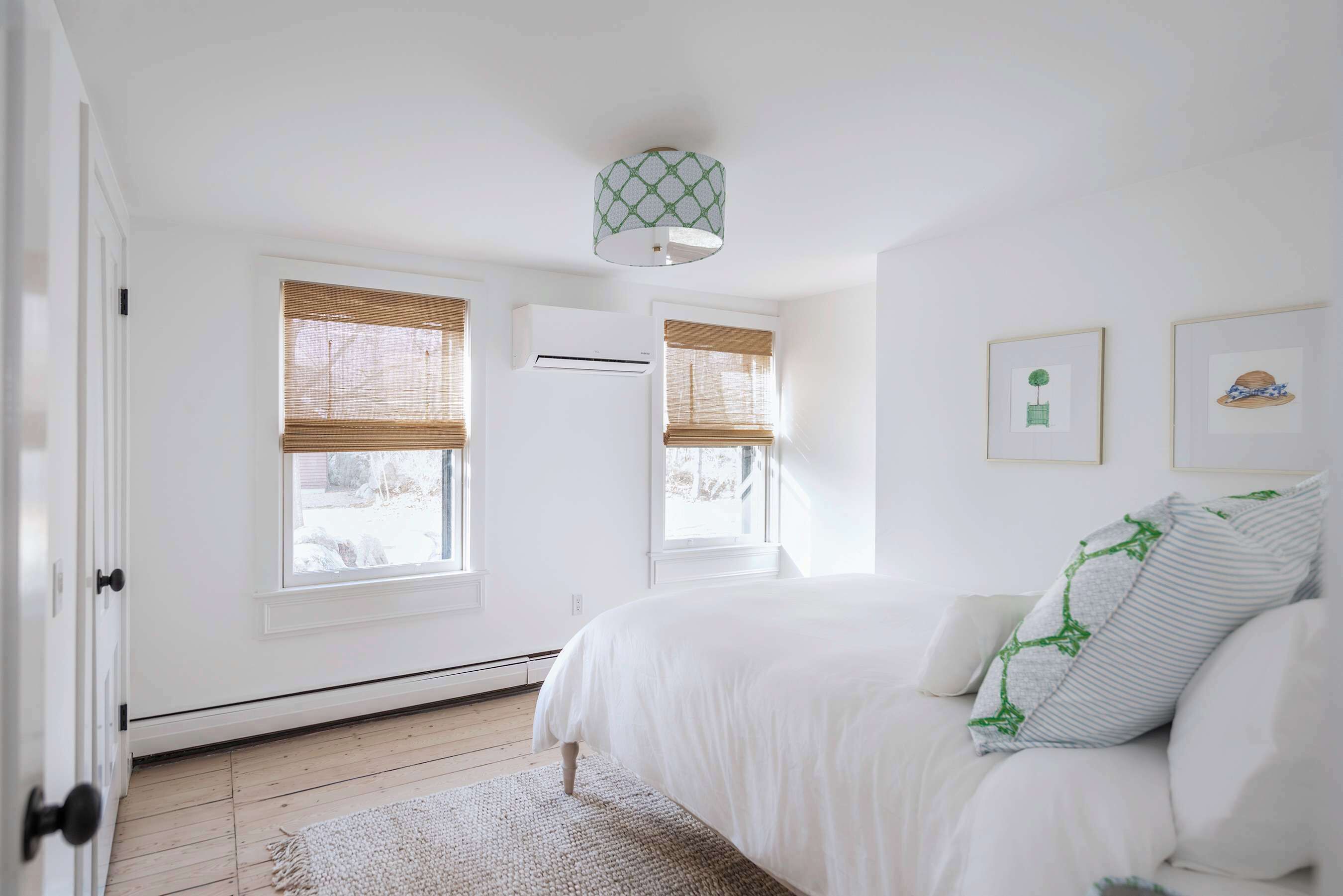 Quarto com cama, janela com persianas, ar-condicionado fixado na parede e luminária no teto.