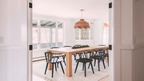 A dining area with a wooden table, black chairs, a woven pendant light, and a white rug. - Good Harbor Beach House (Gloucester)