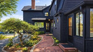 A modern two-story house with a brick pathway leading to the front door, surrounded by a landscaped garden with rocks and shrubs. - Good Harbor Beach House (Gloucester)