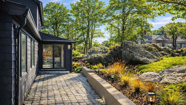 A pathway leading to a building with a glass door, surrounded by a landscaped garden with rocks and plants. - Good Harbor Beach House (Gloucester)
