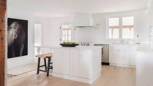 A modern kitchen with white cabinetry, a central island with stools, and a large window. - Good Harbor Beach House (Gloucester)