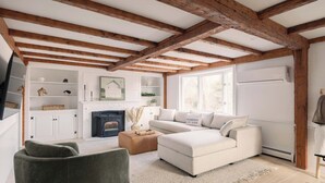 A living room with exposed wooden beams, a fireplace, a sofa, and a television. - Good Harbor Beach House (Gloucester)