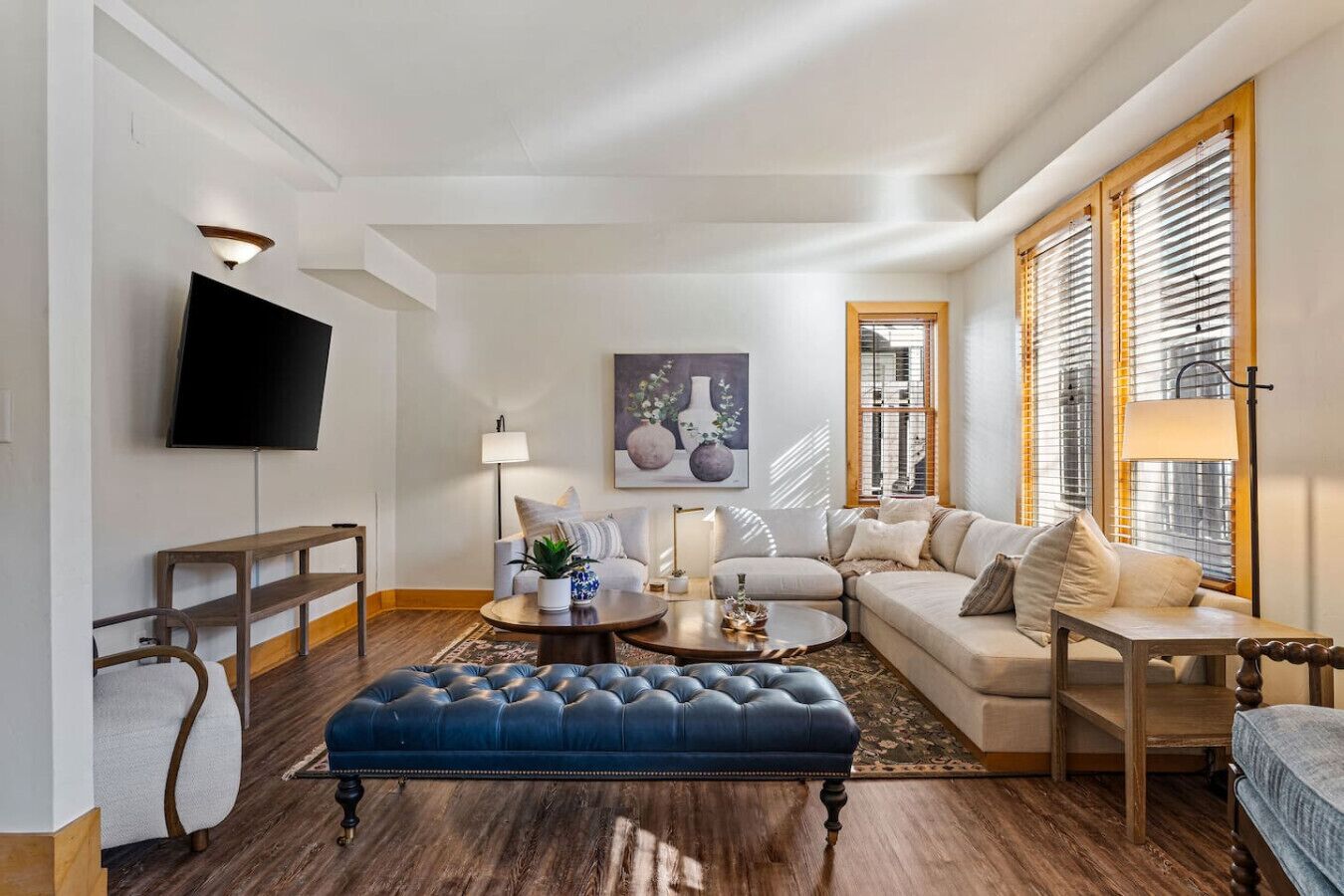 Ein modernes Wohnzimmer mit Sofa, Hocker, Couchtisch und einem an der Wand montierten Flachbildfernseher.
