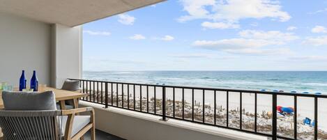 Een balkon met uitzicht op het strand, een tafel met stoelen en een balustrade.