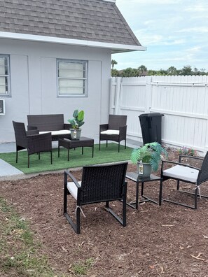 An outdoor patio with wicker furniture, a small table, and potted plants. - Charming Little Nook Near Universal Parks & Outlets. (Orlando)