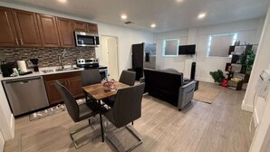 A modern kitchen with wooden cabinets, a microwave, a stove, and a dining area with a table and chairs. - Charming Little Nook Near Universal Parks & Outlets. (Orlando)