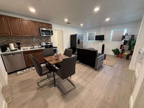 A modern kitchen with wooden cabinets, a microwave, a stove, and a dining area with a table and chairs. - Charming Little Nook Near Universal Parks & Outlets. (Orlando)
