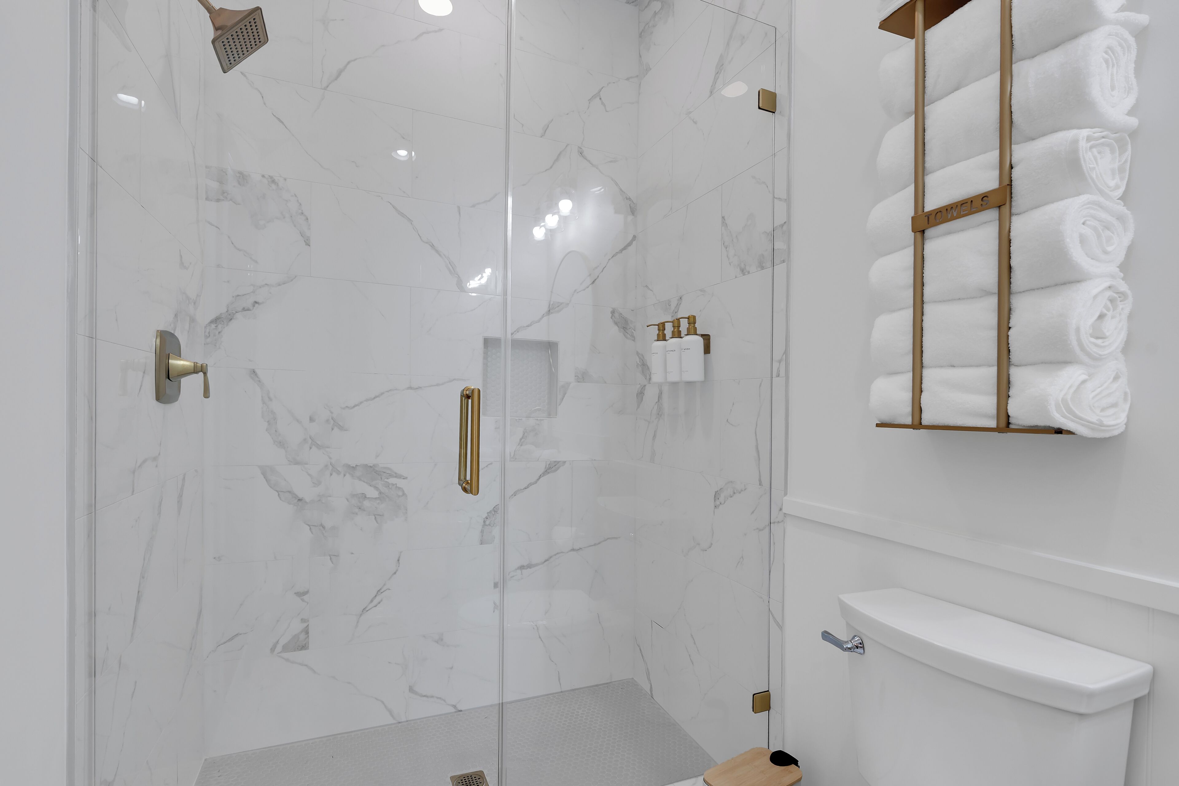 Une salle de bain moderne dotée d’une douche à parois de verre, de murs en marbre et d’un porte-serviettes où sont soigneusement pliées les serviettes.