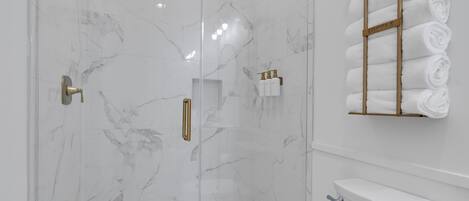 Une salle de bain moderne dotée d’une douche à parois de verre, de murs en marbre et d’un porte-serviettes où sont soigneusement pliées les serviettes.