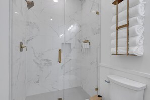 Une salle de bain moderne dotée d’une douche à parois de verre, de murs en marbre et d’un porte-serviettes où sont soigneusement pliées les serviettes.
