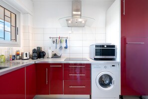 A modern kitchen with red cabinets, a built-in washing machine, and various appliances. - Marius By Terry's Homes (Cannes)