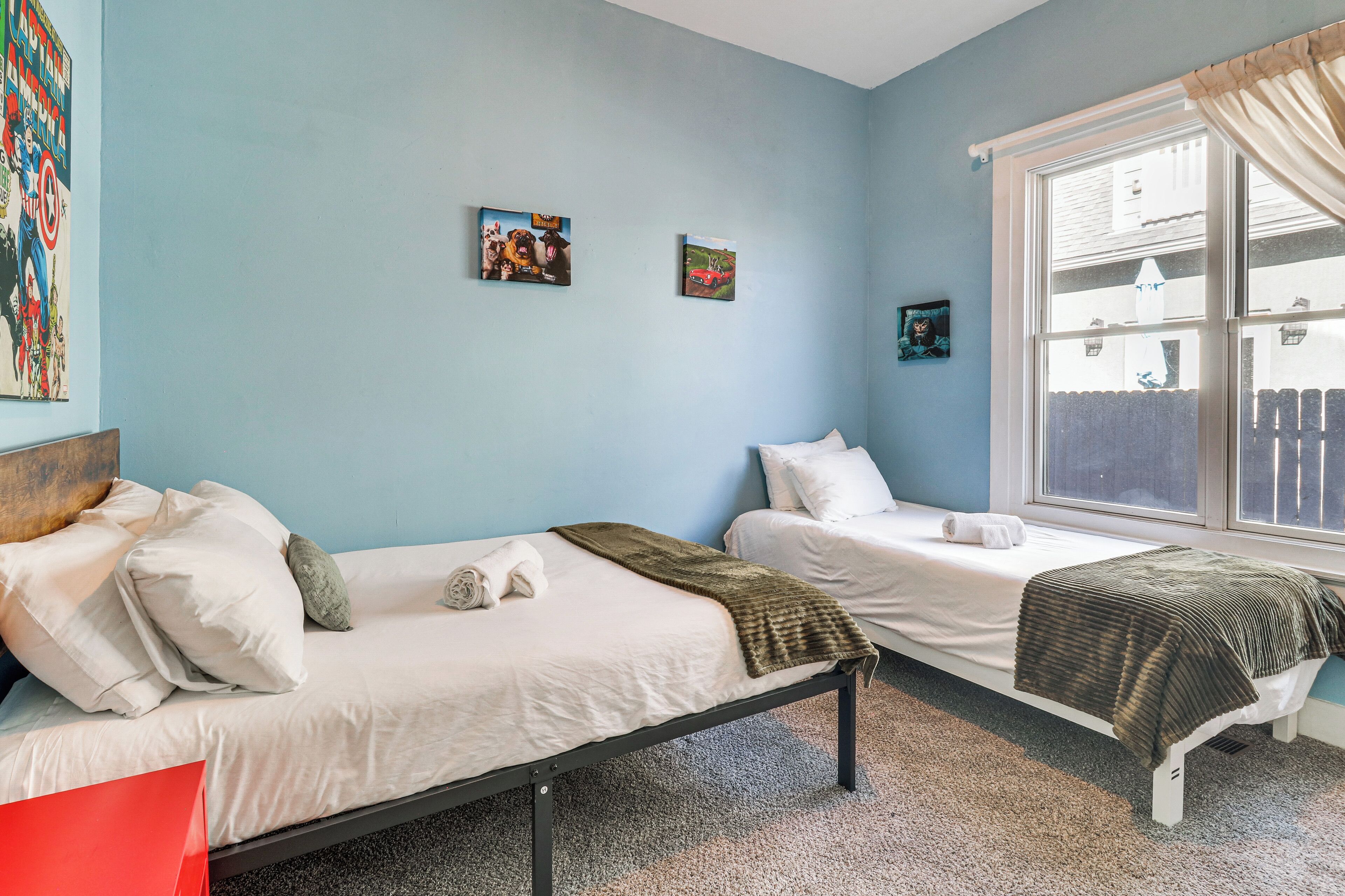 A room with two single beds, a window with curtains, and two wall-mounted pictures.