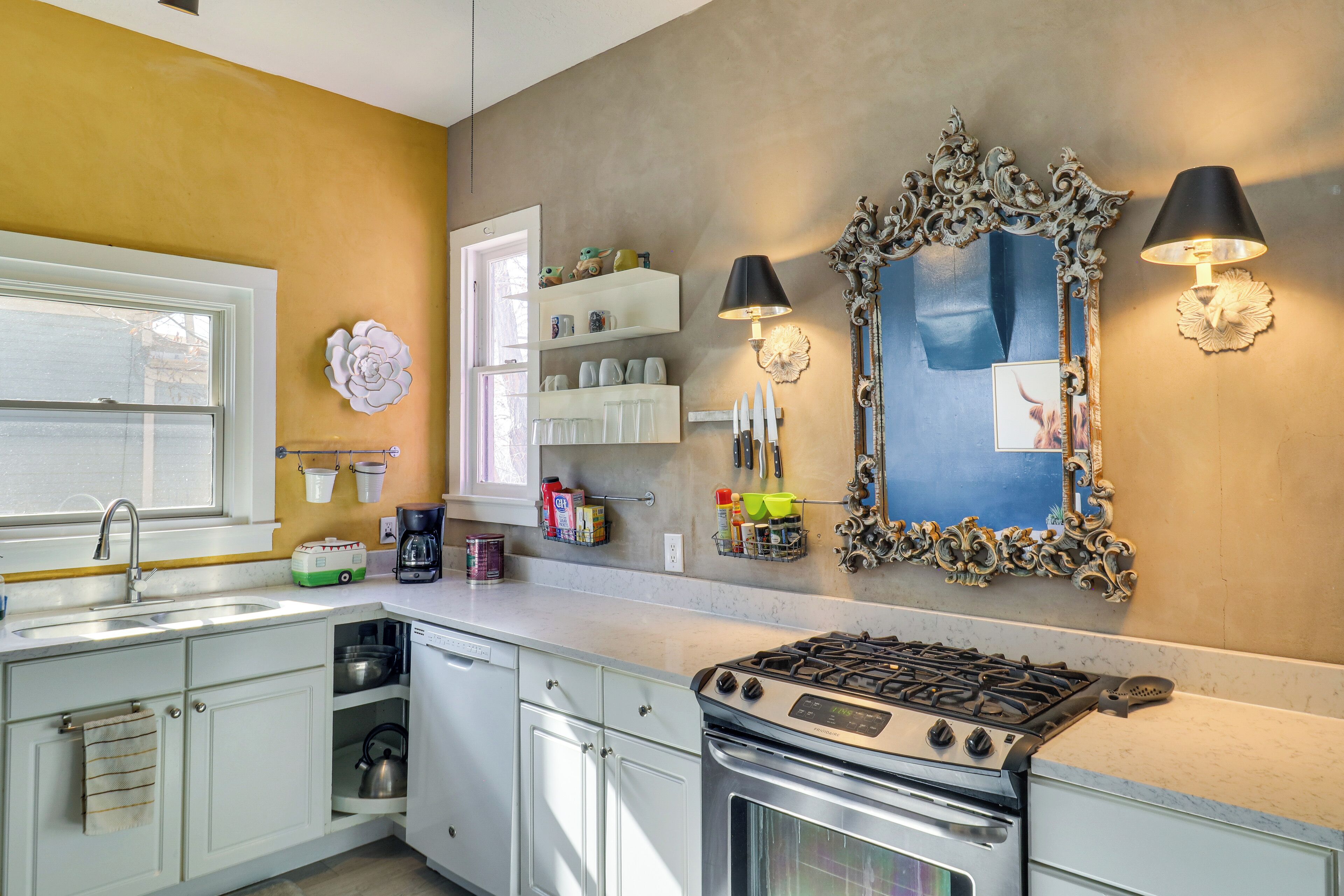 A kitchen with a stove, sink, and cabinets, with decorative wall sconces and a mirror.