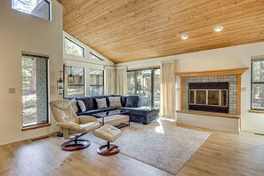 Un salon spacieux avec un plafond en bois, de grandes fenêtres, une cheminée et un canapé d’angle.