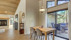 Un vaste espace dédié à la salle à manger, avec une table et des chaises en bois, un luminaire suspendu et une vue sur l’extérieur grâce à de grandes fenêtres.