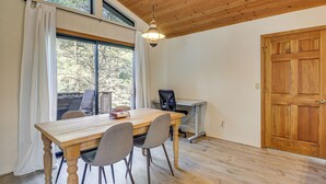 Un espace repas comprenant une table en bois, des chaises, un luminaire suspendu et une vue dégagée sur l’extérieur grâce à de grandes fenêtres.
