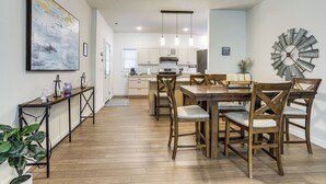 Una cucina moderna con mobili in legno, un tavolo da pranzo con sedie, lampade a sospensione e un grande quadro astratto appeso al muro.